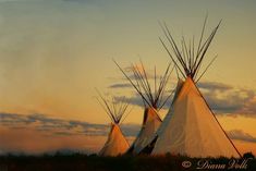 three teepees are standing in the grass at sunset