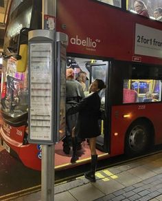 a woman getting on a double decker bus at night