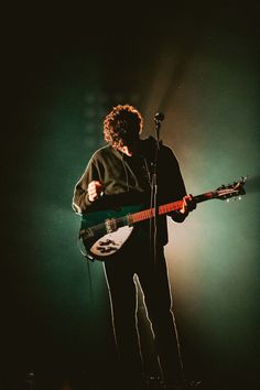 a man standing in front of a microphone while holding a guitar