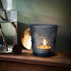 a lit candle sitting on top of a wooden table next to a glass vase and pine cones