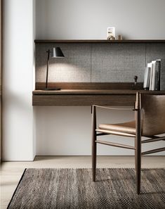 a desk with a chair, lamp and books on it in a white walled room