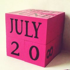 a pink cube with the words july 20 printed on it and two pencils next to it