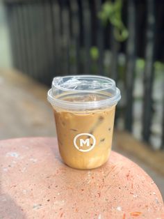 a plastic cup sitting on top of a pink stone table next to a black fence