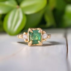 an emerald and diamond ring sitting on top of a wooden table next to green leaves