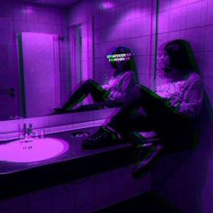 two women sitting on a bathroom counter in front of a purple lit mirror and sink