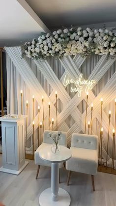 two white chairs sitting next to each other in front of a wall with candles and flowers