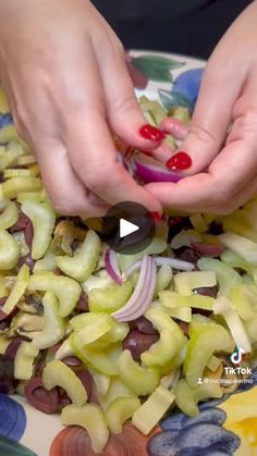 two hands are sprinkling olives into onions on a colorful platter with other ingredients