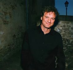 a man in black shirt standing next to a brick wall