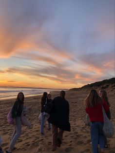 a group of people walking on top of a beach next to the ocean at sunset