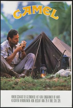 a man sitting in front of a tent eating food next to a lantern and campfire