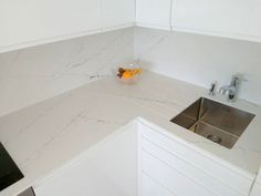 a white kitchen with marble counter tops and stainless steel sink