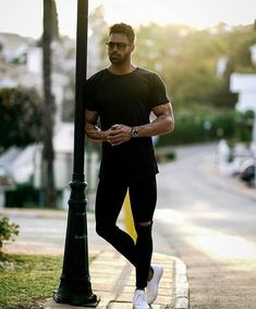 a man standing next to a lamp post on the side of a road with his hands in his pockets