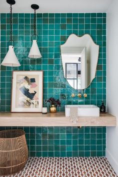 a green tiled bathroom with two sinks and a mirror on the wall, along with hanging lights