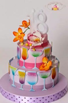 a colorful birthday cake with flowers and wine glasses on the bottom tier is decorated with white frosting