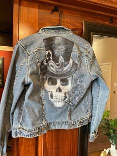 a jean jacket with a skull wearing a hat on it's back hanging from a door