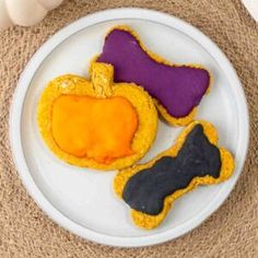 three decorated cookies on a white plate next to some pumpkins and an orange peel