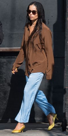 a woman with long hair walking down the street wearing blue jeans and a brown shirt