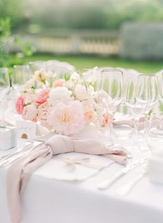 the table is set with wine glasses, napkins and pink flowers on top of it