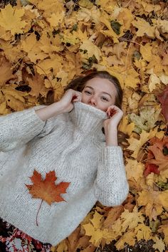 a woman laying on the ground covered in leaves with her hands under her face and looking at the camera