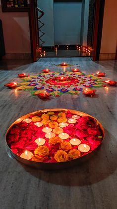 many lit candles are on the floor in front of a tray with flowers and petals