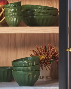 green bowls are stacked on top of each other in front of a wooden shelf filled with apples