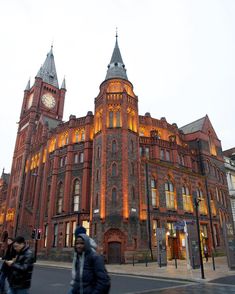 two people walking in front of an old building with a clock on the side of it