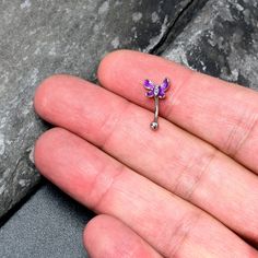 a person's left hand holding a tiny purple flower shaped brooch on top of it