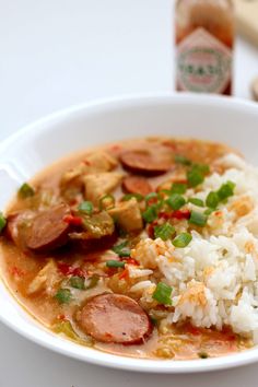 a white bowl filled with rice and sausage on top of a table next to a bottle