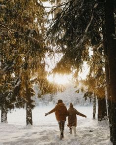 two people are walking through the snow near trees