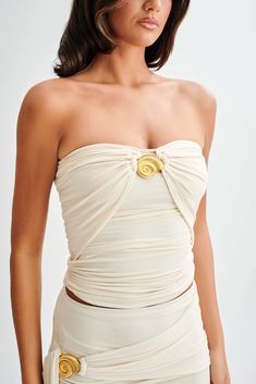 a woman wearing a white dress with gold buttons on the front and side, standing in front of a white background