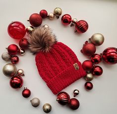 a red hat with a fur pom on it surrounded by christmas balls and ornaments