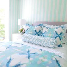 a bed with blue and white comforters in a bedroom next to a striped wall