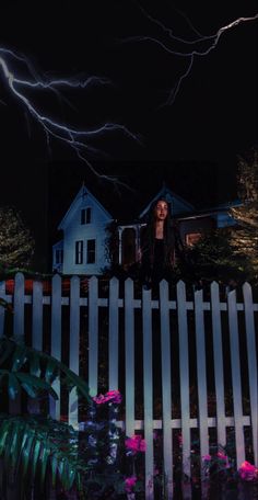 a woman standing in front of a white picket fence at night with lightning behind her