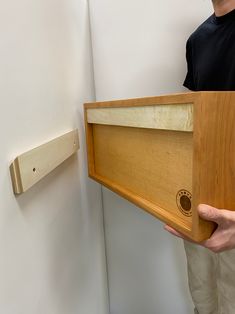 a man holding a wooden object in front of a white wall with a wood frame on it