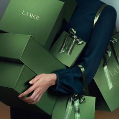 a woman is holding several green boxes with the word la mer written on them in cursive writing