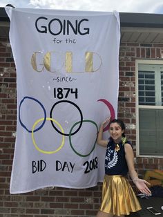 a woman standing next to a sign that says going for the gold since 1974 and bid day 2013