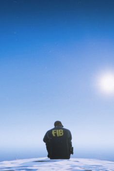 a man sitting on top of a snow covered hill next to the ocean under a bright blue sky