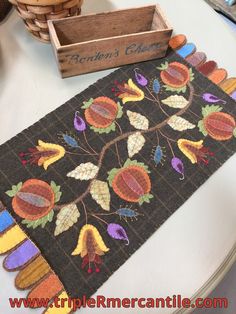 a wooden box sitting on top of a table next to an embroidered place mat with leaves and acorns