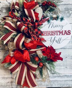 a christmas wreath with red and white bows hanging on a wooden wall next to a sign that says merry christmas y'all