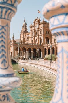 two people in a small boat on the water near a building with arches and pillars