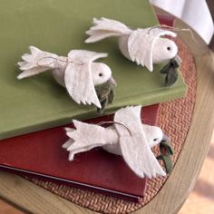 three white birds are sitting on top of some green and red books with leaves attached to them