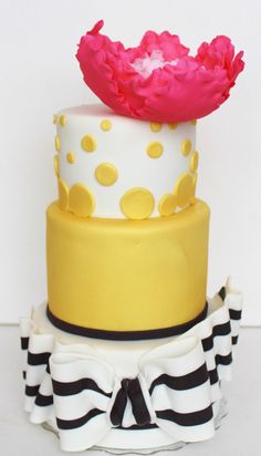 three tiered cake decorated with yellow and pink icing, black and white stripes and polka dots