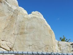 a large rock with carvings on it behind a chain link fence in front of a blue sky