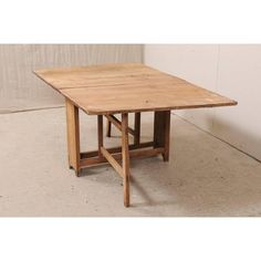 an old wooden table sitting on top of a cement floor next to a white wall