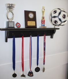 several medals are hanging on a shelf with a soccer ball and trophy in the background