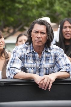 a man with his arms crossed sitting in the back of a truck while people look on