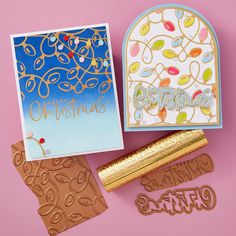 some christmas cards are laying on a pink surface and one has a gold foil stamp