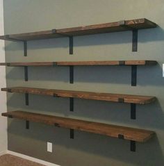 three wooden shelves on the wall in a room with carpeted floor and gray walls