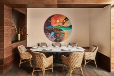 a dining room table with wicker chairs and a round painting hanging on the wall