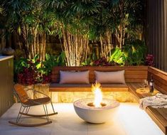 a fire pit in the middle of a patio surrounded by trees and plants at night